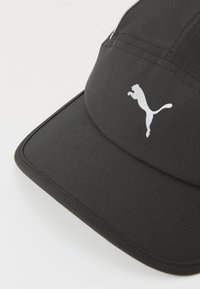 Schwarze Cap mit glatter Textur, mit einem gebogenen Schirm und einem reflektierenden weißen Puma-Logo auf der Vorderseite. Die Nähte sind sichtbar.
