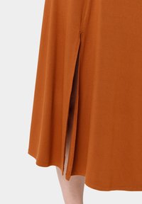 Robe orange brûlé avec une fente sur le côté, confectionnée dans un tissu doux, présentant une texture lisse et un ourlet arrondi.