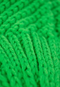 Green knitted fabric featuring textured, raised patterns with visible stitching. The yarn appears soft and fuzzy, creating a cozy appearance.
