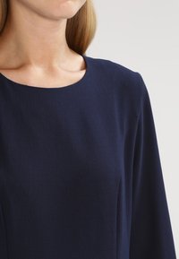 Námořnická modrá blůza s kulatým výstřihem a dlouhými rukávy, vyrobená z hladkého, lehkého materiálu a s jednoduchým, čistým designem.