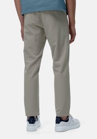 Pantalons beige clair en mélange de coton, avec une coupe droite et une texture subtile. Associés à des baskets blanches et une chemise bleue.