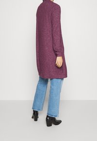 Lång, lös passform, lila stickad cardigan med en strukturerad yta, med långa ärmar och rundad halsringning, kombinerad med ljusblå denimjeans.