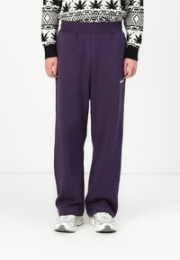 Purple sweatpants with a relaxed fit, made of soft fabric. Features a wide waistband and small logo detail on the side.