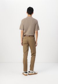 Polo à manches courtes, beige, en tissu texturé, associé à un pantalon slim fit marron clair et des baskets blanches avec des accents noirs.