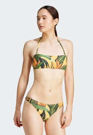 Completo bikini con una base gialla decorata con motivi di foglie e fiori tropicali. Il top ha un design bandeau con spalline regolabili; il fondo è a vita bassa.