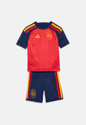 Red short-sleeve soccer jersey with navy sleeves and yellow stripes, paired with navy shorts featuring red and yellow side stripes and a crest.
