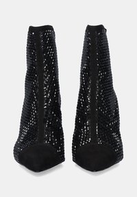 Botas negras hasta el tobillo con un diseño de malla texturizada con formas de pirámide, punta afilada y un cierre de cremallera en la parte trasera. Acento de ante suave en la punta.