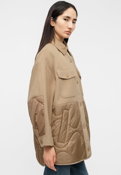 Μπεζ γιλέκο με καπιτονέ λεπτομέρειες, κατασκευασμένο από μίγμα μαλλιού και σατέν, με μπροστινές τσέπες και διακοσμητικά κουμπιά, που αναδεικνύει μια χαλαρή σιλουέτα και υφή.