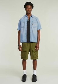 Ljusblå denimskjorta med kort ärm och två bröstfickor, ihopparad med olivgröna cargoshorts som har stora framfickor. Svarta skor och en svart T-shirt under.