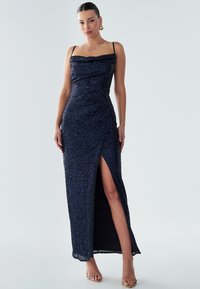 Glänzendes navy Maxi-Kleid mit figurbetonter Silhouette, drapiertem Ausschnitt und seitlichem Schlitz. Feine Textur mit schmalen Spaghettiträgern und betontem Taillenbereich.