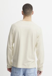 Koszula z długim rękawem w kolorze kremowym, wykonana z teksturowanej tkaniny. Posiada okrągły dekolt i luźny krój. Prosty i minimalistyczny design.