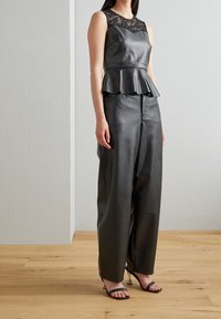 Top peplum in pelle nera con scollatura in pizzo. Abbinato a pantaloni larghi in pelle nera e tacchi neri con fasce. Texture liscia.