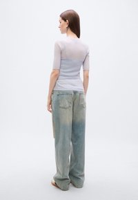 Ανοιχτόμωβ ριμπ πλεκτό τοπ με κοντά μανίκια, συνδυασμένο με ξεθωριασμένο τζιν φαρδιάς ραφής. Το σύνολο έχει χαλαρή σιλουέτα και μινιμαλιστικό σχεδιασμό.