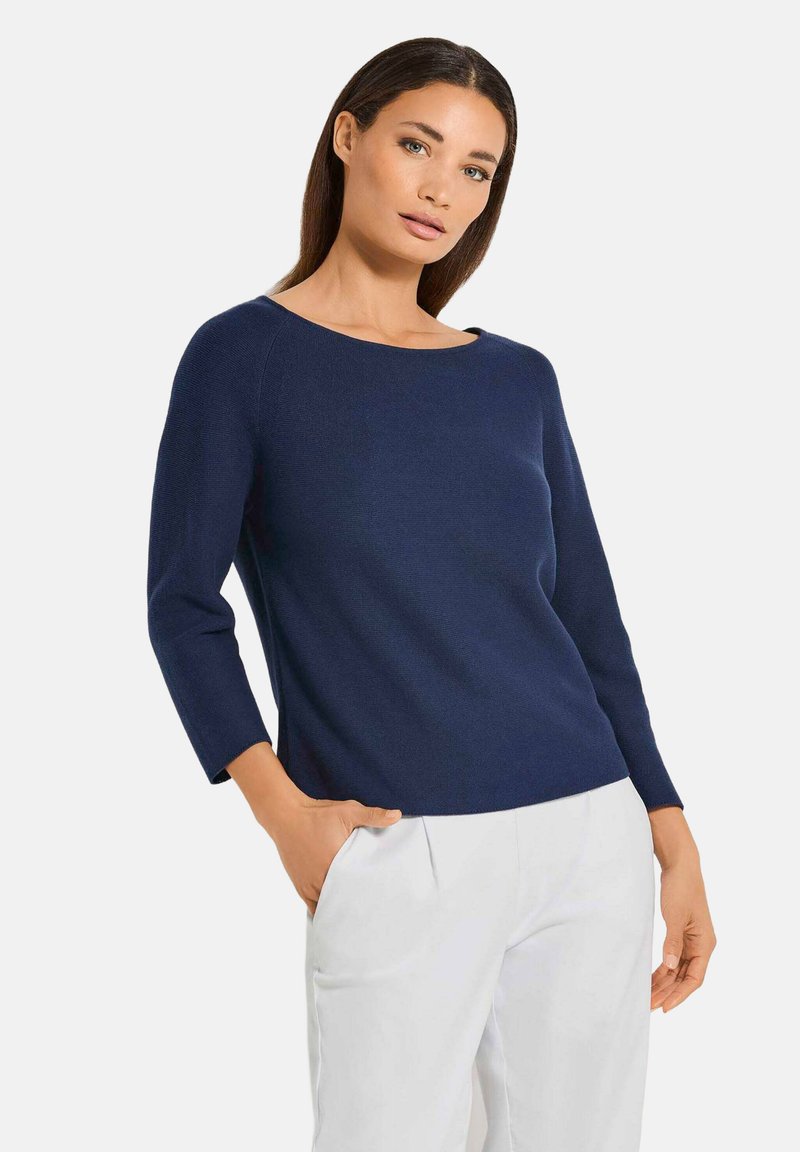 Marineblauer Strickpullover mit Rundhalsausschnitt und 3/4-Ärmeln. Glatte Textur und lockere Passform, kombiniert mit weißen Hosen.