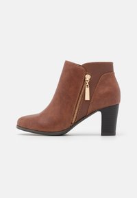 Bottine marron en similicuir avec une fermeture éclair latérale, des accents texturés et un talon empilé. Caractérisée par un bout arrondi et une silhouette élégante.