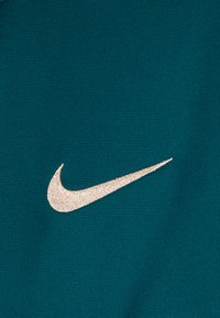 Tessuto atletico color turchese con un prominente logo Nike in beige ricamato. Superficie testurizzata con un sottile motivo a griglia.
