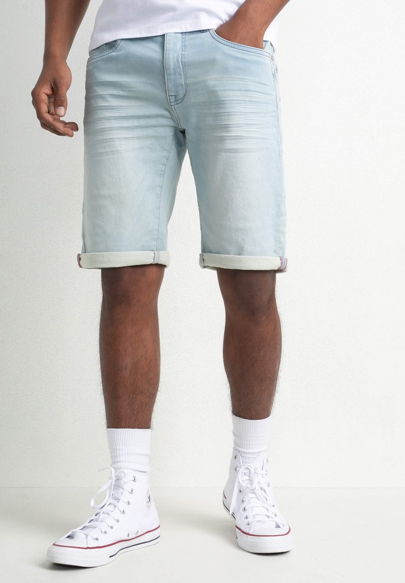 Ljusblå denimshorts med uppvikta avslut, framfickor och lätt blekning. Bärs med vita sneakers och ankelsockor.