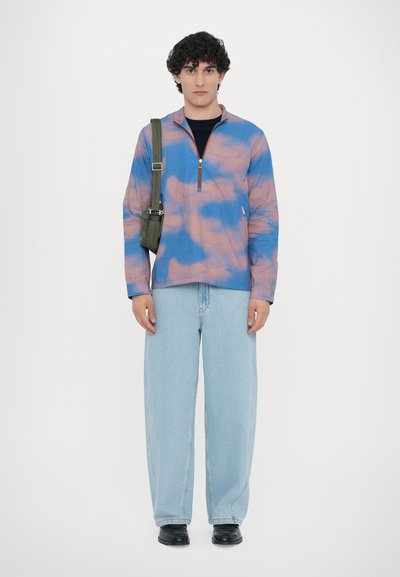 Blue and pink tie-dye zip-up jacket, relaxed fit, paired with light blue baggy jeans and black shoes, with a green crossbody bag.