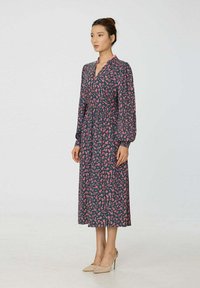 Robe midi bleue à fleurs avec manches longues, encolure en V et taille froncée. Comprend des motifs floraux roses et un tissu doux.