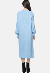 Abito lavorato a maglia azzurro chiaro con maniche lunghe, scollatura a coste e motivo testurizzato sul retro. Lunghezza a metà polpaccio con una vestibilità rilassata.