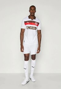 Valge jalgpallikomplekt punaste ja pruunide horisontaalsete triipudega. Komplekti kuulub pruun krae, valged lühikesed püksid ja sobivad sokid mustade logode aktsentidega.