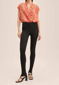 Blusa a maniche corte con scollatura a V in un motivo ondulato rosso e rosa, abbinata a leggings neri a costine e sandali neri con tacco a listini.