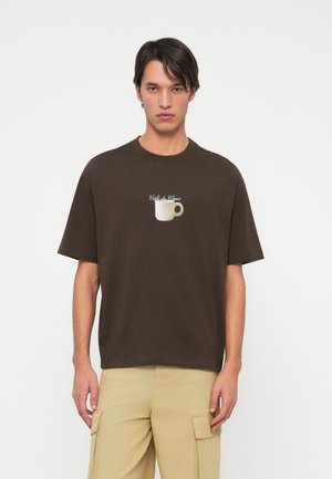 Camiseta de algodón marrón de manga corta, con un gráfico de una taza de café en blanco y texto que dice "Café de Choux" en cursiva.