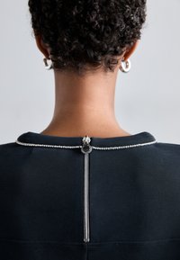 Prenda negra con cierre de cremallera en la parte posterior, acentuada con una fila de rhinestones transparentes a lo largo del escote. Textura de tela suave.