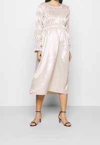 Ljusrosa satin klänning med långa, puffiga ärmar och elastisk midja. Tyget har en slät, glänsande textur och når till halva vaden.