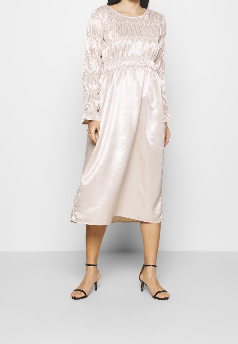 Ljusrosa satin klänning med långa, puffiga ärmar och elastisk midja. Tyget har en slät, glänsande textur och når till halva vaden.
