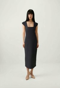 Rochie midi închisă la culoare, cu decolteu pătrat, mâneci scurte și siluetă ajustată, realizată dintr-un material neted. Asortată cu pantofi cu toc bej.