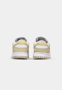 Nike Dunk Low tenisky s bielou koženou hornou časťou a žltými semišovými akcentmi, s textúrovanou tkaninou a gumovou podrážkou.