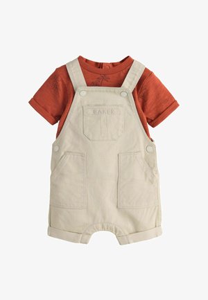 Beige Baumwoll-Latzhosen für Kleinkinder mit Vordertaschen über einem rostfarbenen Kurzarmshirt mit dezenten Palmenmustern.