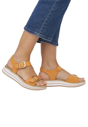 Sandali in pelle marrone chiaro con punta aperta, cinturini regolabili con fibbia e una suola platform bianca con fondo texturizzato per una maggiore aderenza.