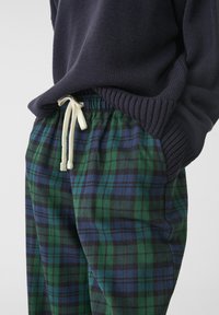 Puuvillaiset ruudulliset housut, joissa on vihre�ä, sininen ja musta ruutukuosi, joustava vyötärö valkoisella nyörillä ja rento istuvuus.
