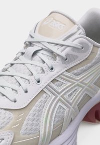 Λευκό και μπεζ παπούτσι ASICS για τρέξιμο με άνω μέρος από δίχτυ, λευκά κορδόνια και χαρακτηριστικό λογότυπο ASICS στο πλευρό και τη γλώσσα, κοντινή όψη.