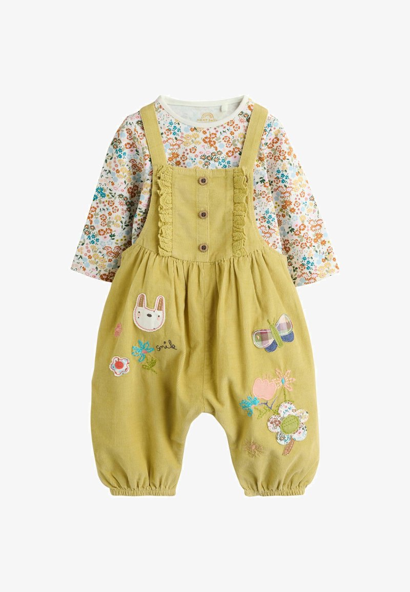 Barboteuse bébé jaune en velours côtelé avec boutons, broderies florales et animales, portée sur une chemise blanche à manches longues à motif floral.