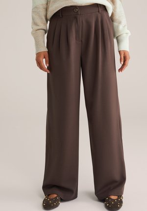 Bruine wijde broek met plooien, voorzien van een knoopsluiting en een gladde stoftextuur. Gedragen met een lichtgekleurde gebreide trui.