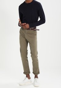 Jersey de manga larga color navy con cuello redondo, combinado con chinos caqui y zapatillas blancas. Los chinos tienen los puños doblados y un cinturón marrón.