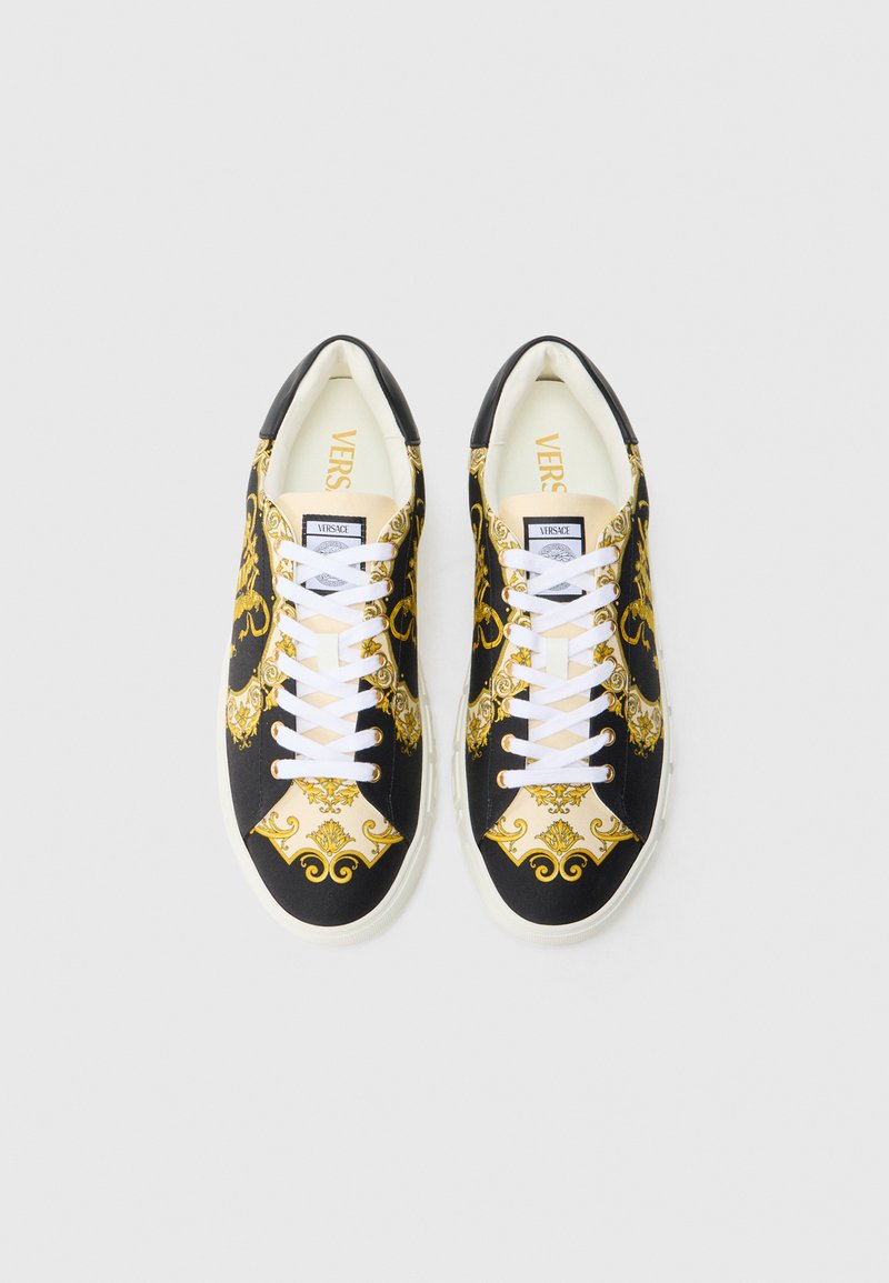 Schwarze und goldene Sneaker mit gemustertem Design, weißen Schnürsenkeln und kontrastierender weißer Sohle. Innen mit "VERSACE"-Markenlogo versehen.