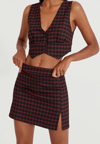Haut court en plaid noir et rouge avec un décolleté en V profond, devant à boutons, et jupe mini assortie avec une fente sur le côté et une texture lisse.