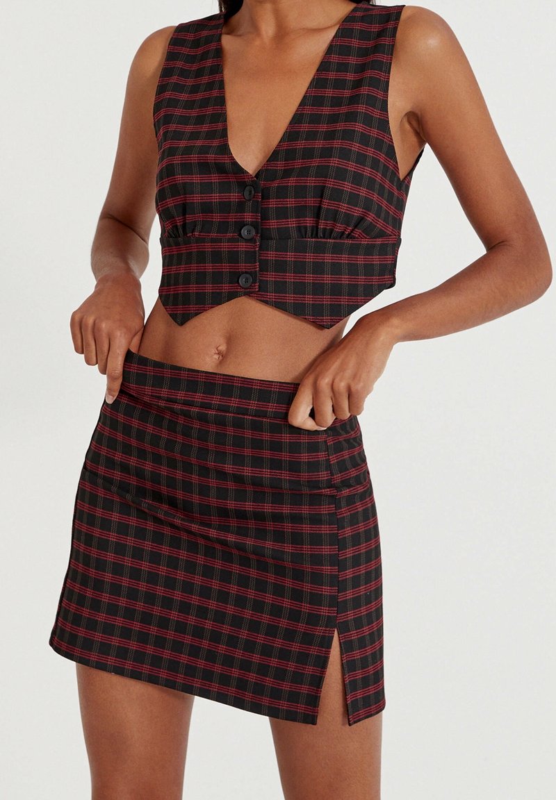 Haut court en plaid noir et rouge avec un décolleté en V profond, devant à boutons, et jupe mini assortie avec une fente sur le côté et une texture lisse.