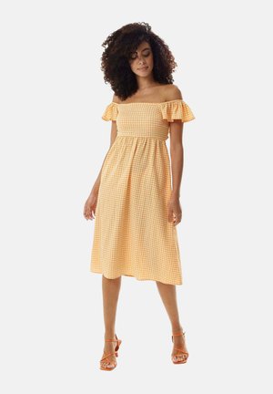 Off-the-shoulder yellow gingham dress with ruffled sleeves, a fitted bodice, and flared skirt, paired with orange strappy heels.