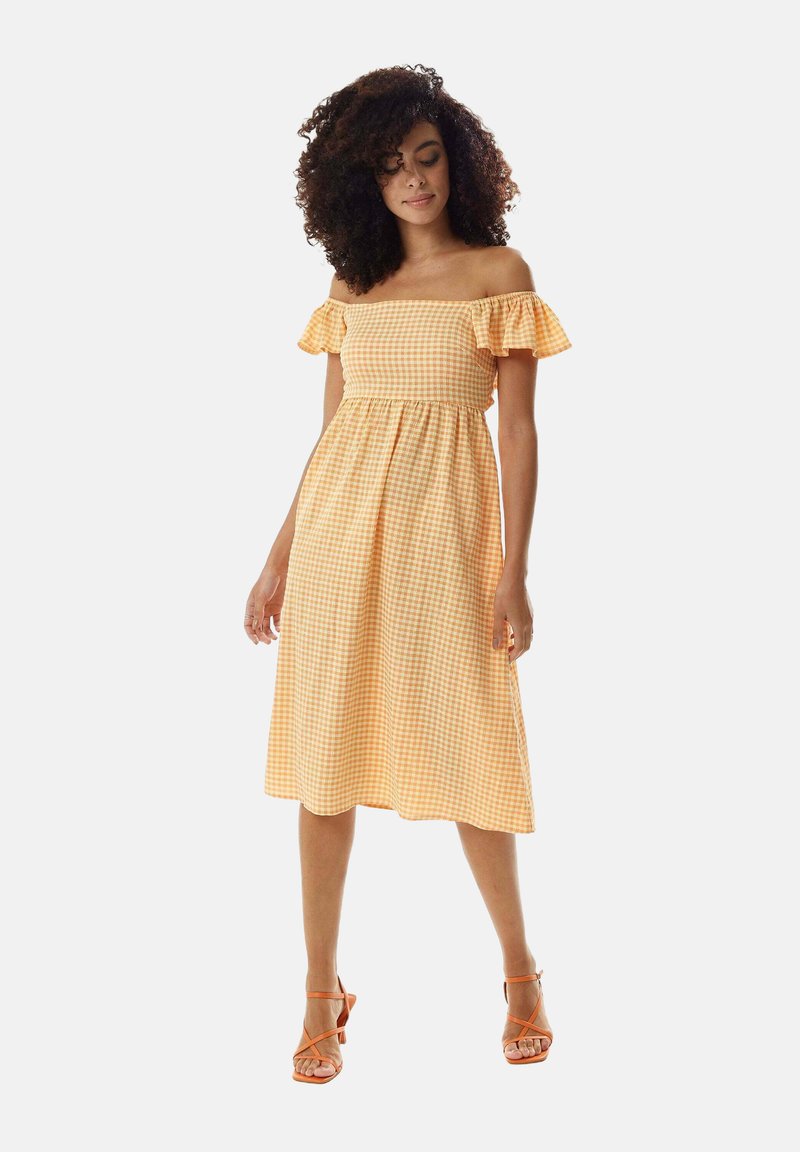 Off-the-shoulder yellow gingham dress with ruffled sleeves, a fitted bodice, and flared skirt, paired with orange strappy heels.