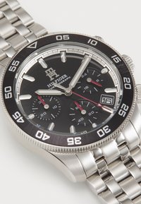 Edelstahl-Chronographenuhr mit schwarzem Zifferblatt, silbernen Stundenmarkierungen und roten Akzenten. Verfügt über eine drehbare Lünette und ein Gliederarmband.