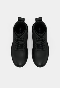 Bottines noires en cuir avec lacets, surface texturée, tirette au niveau du talon et design à bout rond. Nom de la marque visible à l'intérieur.