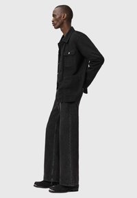 Czarna dżinsowa kurtka z kołnierzem, dwoma kieszeniami na piersi i guzikami, zestawiona z szerokimi, ciemnoszarymi spodniami dżinsowymi i czarnymi butami.