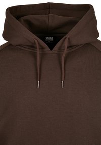 Sudadera marrón con capucha ajustable, cuenta con un cuello y puños acanalados, elaborada en un tejido suave. La etiqueta dice "URBAN CLASSICS M."