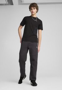 Czarna koszulka sportowa z zamkiem, zestawiona z szarymi dresami. Spodnie mają zaokrąglone szwy i logo PUMA. Czarnych sneakersów dopełniają całość.