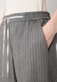 Pantalons rayés gris avec une taille élastiquée et un cordon de serrage. Présente des poches latérales et un accent logo sécurisé près de la taille.